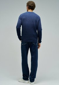 Maglione blu navy con un motivo testurizzato, abbinato a jeans scuri e sneakers bianche. Vista dalla schiena, che evidenzia la vestibilità e il colore.