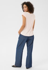 Un haut rose clair à manches courtes associé à un pantalon en denim bleu foncé à coupe ample. La tenue présente une silhouette décontractée et une texture lisse.