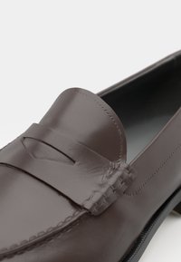 Brune skinn loafer med en glatt finish, med en sydd aksent på tåen og en avrundet overdel. Sålen har svart detaljer.