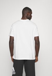 Bela bomba iz bombaža s kratkimi rokavi in okroglim ovratnikom, ki ima gladko teksturo in sproščen kroj. Zadnji pogled prikazuje preprostost v dizajnu.