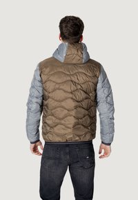Brun og grå puffjakke med hætte, der har quiltningsstrukturer og et design, der kombinerer to forskellige farver og materialer.