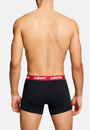 Mann von hinten, der schwarze Levi’s Boxer mit rotem Bund und weißem Logo vor einem einfarbigen weißen Hintergrund trägt.