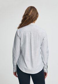 Camicia a righe con strisce verticali grigie e bianche, maniche lunghe, orlo arrotondato e bottoni sui polsini. Vista posteriore mostrata.