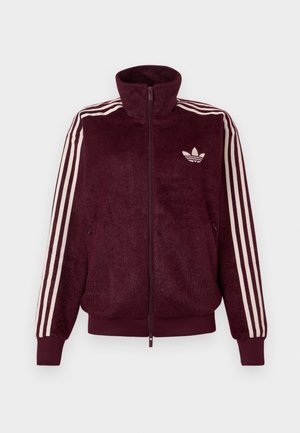 Burgundi värvi sametist tõmbluku kangasjakk, millel on kolm valget triipu varrukatel ja valge Adidas'i kolmnurk-logo vasakul rindkerel.