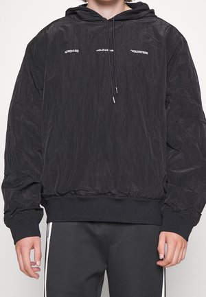 Black hooded sweatshirt made from textured material, featuring printed text, elastic cuffs, and a drawstring at the neckline.