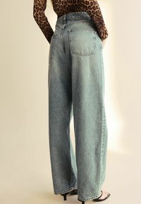 Långbenade denimjeans i ljusblått, med hög midja, bakfickor och en tvättad textur. Bärs med svarta högklackade sandaler.