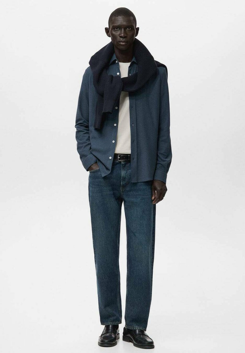 Blå skjorte med knapper, hvid t-shirt, mørkeblå jeans, marineblå strikket tørklæde, sorte sko. Slim fit, glat stof, enkelt design, ingen mønstre.