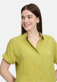 Limoengroene kortemouwenoverhemd van lichtgewicht stof, met een kraag, knopenlijst en opgerolde mouwuiteinden met een gladde textuur.