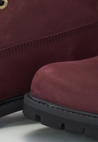 Bordeaux-farbene Wildleder-Stiefeletten mit runder Zehenpartie, strukturierter Oberfläche und einer schwarzen Gummisohle mit tiefen Profilmustern.