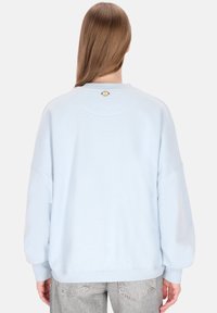 Lichtblauwe oversized trui met een ronde halslijn, doorlopende schouders en een klein geel logodetail op de achterkant. Gemaakt van een katoenmix.