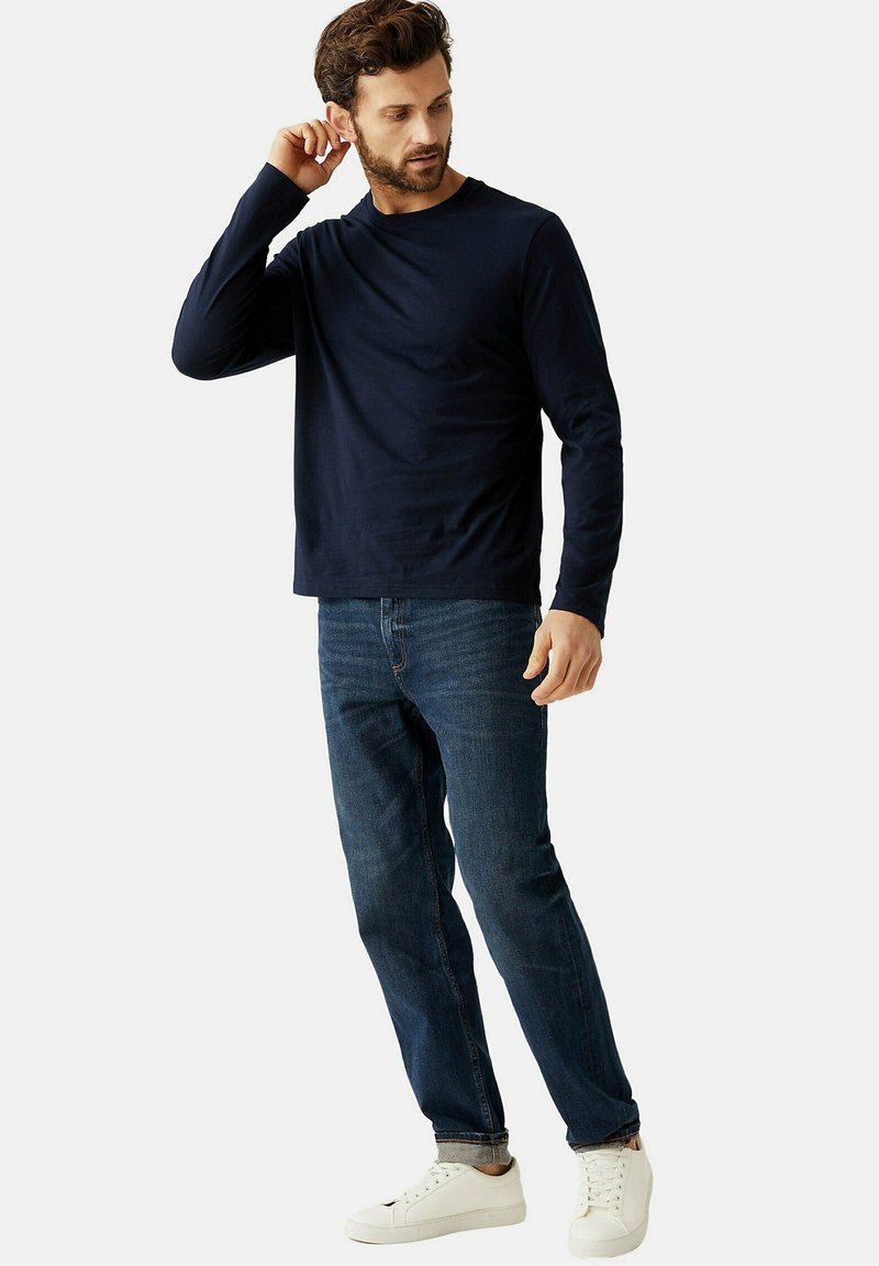Dunkelblaues Langarm-Shirt mit Rundhalsausschnitt, kombiniert mit dunkelblauen Jeans und weißen Sneakers, was ein lässiges Outfit ergibt.