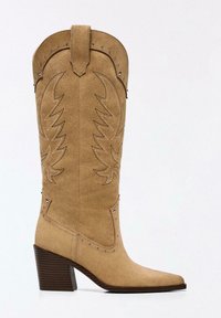 Suede cowboy boot in light brown with pointed toe, decorative stitching, and silver-tone studs on the sides. Chunky wooden heel.