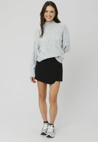 Un pull en tricot gris clair et confortable avec un col haut, associé à une jupe noire de style portefeuille. Le modèle porte des chaussures de sport grises.