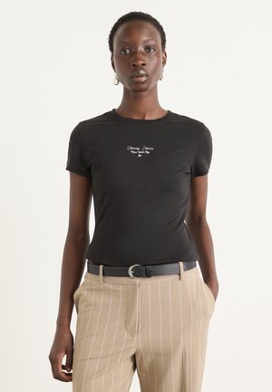 Czarna dopasowana koszulka z krótkimi rękawami z białym napisem "Tommy Jeans New York City", zestawiona z beżowymi spodniami w prążki i czarnym paskiem.