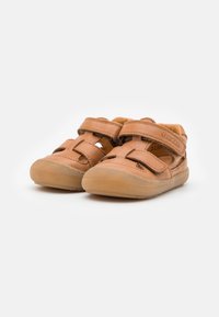 Brown leather toddler shoes with two Velcro straps, open sides, and a rubber sole. Rounded toe and stitched accents.