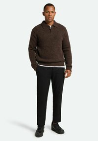 Brun strikket polo sweater med krave, to knapper, parret med sorte bukser og sorte sneakers. Enkel, tekstureret stof.