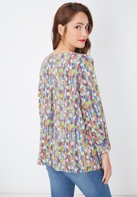 Blusa de estampado colorido que presenta una variedad de diseños de hojas, con mangas largas y un corte holgado, combinada con jeans de color azul claro.