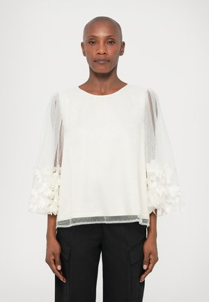 Bela majica s kratkimi, prosojnimi pufastimi rokavi, okrašenimi s cvetličnimi detajli na zapestjih. Gladka tkanina z pikčasto teksturo.