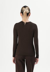 Persoană cu o coadă de cal blondă, purtând un top mulat cu mânecă lungă de culoare maro închis și pantaloni de leopard maro închis, văzută din spate.