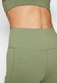 Olive green seamless sports bra and matching high-waisted leggings. Smooth texture, minimalist design, and no visible hardware or patterns.