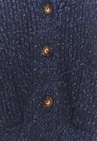 Zbliżenie na ciemnoniebieską dzianinę z pionowym prążkowaniem i trzema brązowymi marmurkowymi guzikami umieszczonymi na środku.