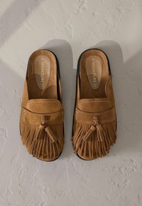 Zapatos de ante marrón tipo slip-on con un diseño con flecos y detalles de borlas, suelas de goma negras y costuras en contraste.