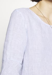 Blusa a righe blu chiaro, realizzata in tessuto testurizzato, con scollo ampio e maniche a tre quarti. Visibili dettagli di filo in contrasto.