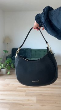 Črna usnjena torba s poševno obliko, z zlatimi kovinskimi detajli in vidnim logotipom. Podrobnosti vključujejo zadrgo in ozak ramenski trak.