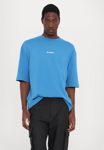 Blå oversized t-shirt i bomull med korta ärmar. Har en minimalistisk textlogotyp i vitt på bröstet. Matchar med svarta cargobyxor.
