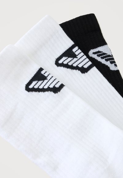Trois chaussettes côtelées crew, deux blanches et une noire, chacune avec un logo flèche rayé noir et blanc près du revers.