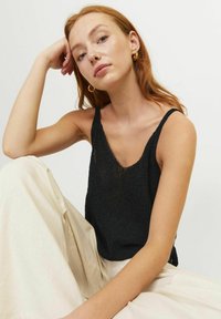 Top sin mangas de punto negro con escote en V, tirantes finos y un corte holgado, combinado con pantalones de pierna ancha en un tono beige claro. Textura suave y diseño casual.