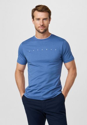 Camiseta de algodón azul con mangas cortas, cuello redondo, con texto blanco "HACKETT" en el pecho; textura suave y diseño ajustado.