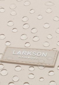 Water droplets on beige textured fabric with a beige rectangular label reading "LARKSON HAMBURG" in white letters.