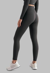 Mørkegrå ribbede leggings med høy midje, fitted design og sømløse detaljer, kombinert med hvite treningssko.