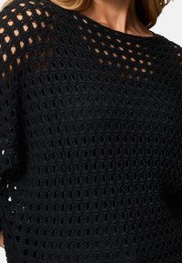 Haut noir en tricot avec un motif ajouré. Doté d'un large décolleté et de manches courtes. Texture douce avec un design léger.