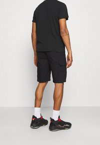Shorts cargo noirs avec de multiples poches, portés avec un t-shirt noir, des chaussettes blanches et des chaussures de sport noires avec des accents rouges et verts.