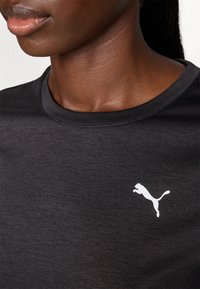 Juoda sportinė marškinė su apvaliu iškirpimu, pagaminta iš lygios medžiagos, su baltu Puma logotipu kairėje krūtinės pusėje.