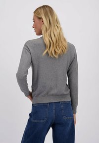 Grijze gebreide trui met een ronde halslijn en lange mouwen, met een geribbelde zoom. Getoond in combinatie met donkerblauwe spijkerbroek.