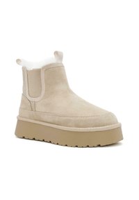 Stivaletto in suede beige con un morbido rivestimento bianco, pannelli laterali elastici e una suola spessa e chunky beige con battistrada testurizzato.
