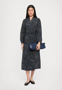Dark floral-print long dress with long sleeves, belted waist, and fitted cuffs. Accompanied by a textured blue clutch and black flats.