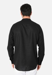 Maglietta nera a maniche lunghe realizzata in tessuto morbido, con colletto a camicia e orlo dritto; superficie testurizzata senza motivi visibili.