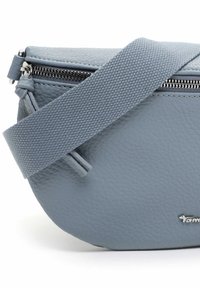 Sac banane en cuir gris clair avec une forme arrondie, une surface texturée, une fermeture éclair en métal et une bandoulière en tissu tissé. Comprend un détail de logo.