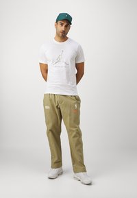 Fehér póló, színes Jumpman logóval. Olívazöld nadrág, NBA és Nike logóval, oldalán patent gombokkal. Fehér cipő.