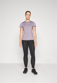 Light purple short-sleeve athletic top paired with black leggings. Top is smooth; leggings are stretchy with a subtle pattern along the side.