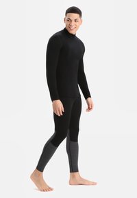 Fekete hőszigetelő, hosszúujjú felső és testhezálló leggings, szürke kiegészítőkkel az alsó lábszáron. Nyújtható anyagból készült a melegség és kényelem érdekében.