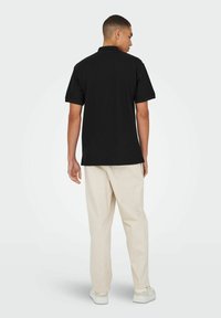Sort kortærmet polo skjorte med klassisk krave, parret med lyse, løstsiddende bukser og hvide sneakers.