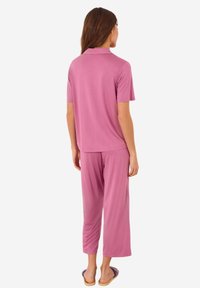 Korte roze pyjama set met een polo-stijl top en losvallende broeken. Soepele textuur, lichte stof en pant lengte tot halverwege de kuit.