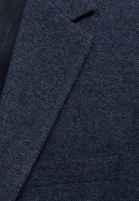 Granatowa, teksturowana tkanina o diagonalnym wzorze prążkowania, z ostrym kołnierzem i widocznym małym detalem kieszeni.