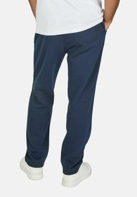 Marineblauwe joggingsbroek van katoenmix met een rechte pasvorm, voorzien van zijzakken en een elastische tailleband, gecombineerd met witte sneakers.