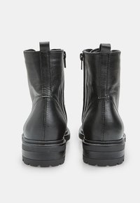 Stivali ankle in pelle nera con finitura texturizzata, suola bassa e spessa, e cerniere laterali per una facile calzata. Tallone rinforzato e design minimale.